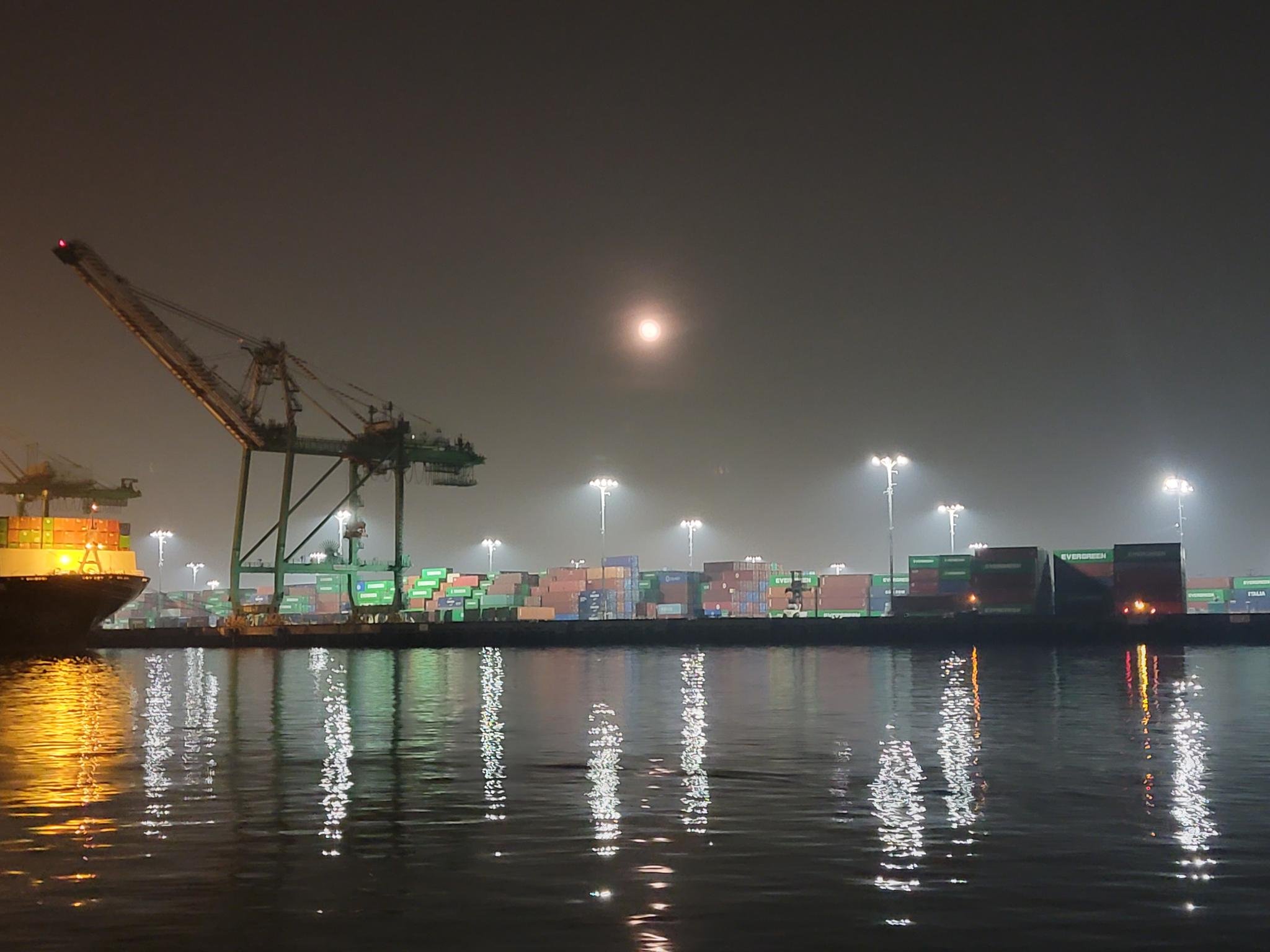 A series of shipping containers on a dock with floodlamps illuminating them.