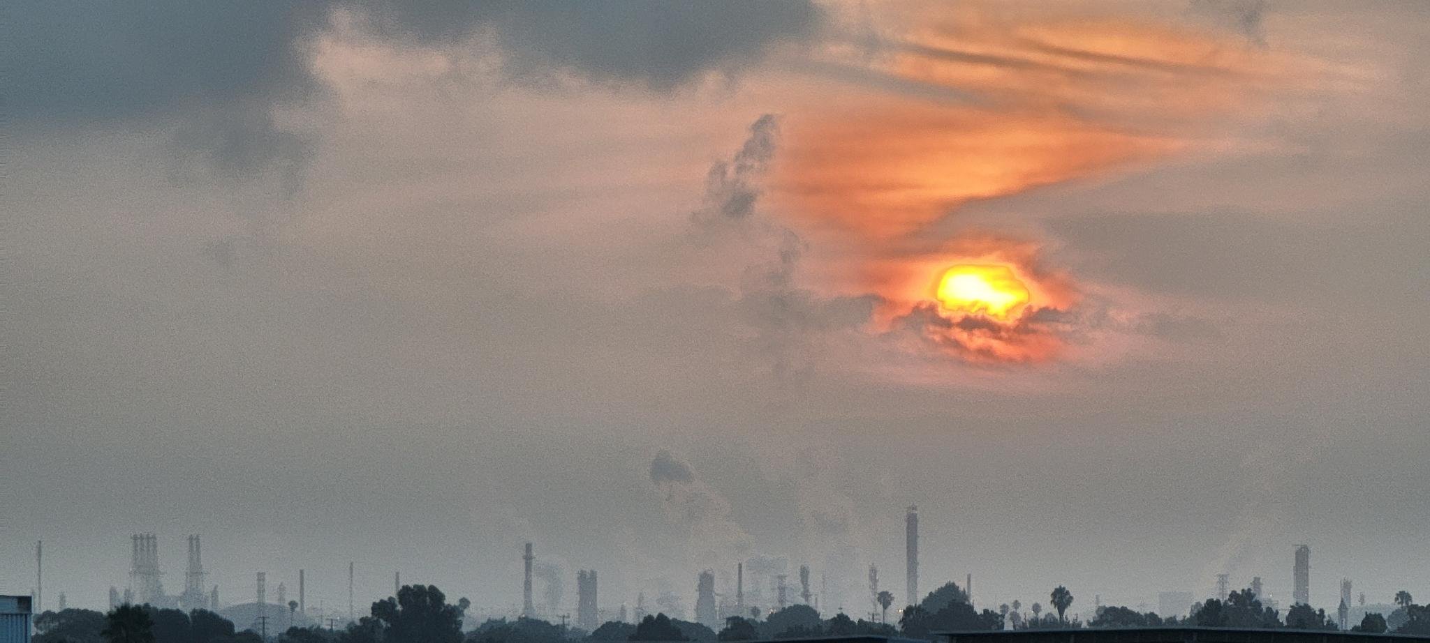 An oil refinery with the sun in the background leaving red straks in the clouds.